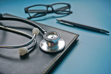 Business and Medical concept. Stethoscope on black organizer. Eye glasses and pen on blue background.