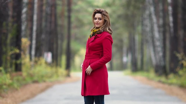 portrait of a young woman in an autumn park. beautiful girl in red coat posing and smiling at the camera