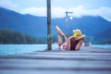 girl in a hat sitting on a long wooden pier in the evening