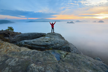 Obraz premium Hiker on rock end above valley. Man watch over misty and autumnal morning valley to bright morning Sun.