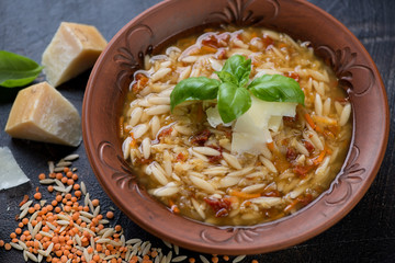 Closeup of italian soup with lentils and pasta served in a clay plate, selective focus