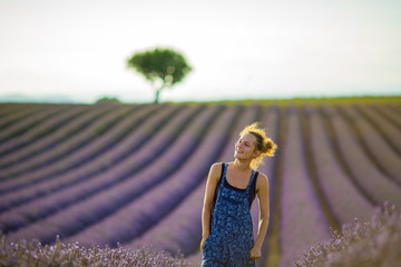 girl farmer in overalls bent her head under the rays of the evening sun, standing in the midst of a ripening lavender field