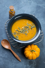 Plate of pumpkin cream-soup with pumpkin seeds and spices on a cooling rack, studio shot