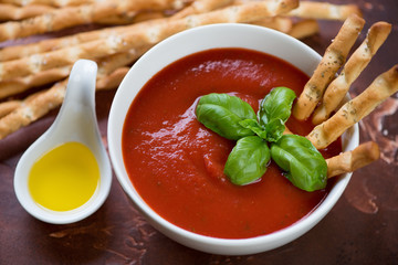 Bowl of gazpacho soup served with salted bread sticks, close-up, selective focus