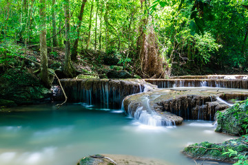 Tranquil waterfall and pool shaded by tropical jungle plants in Erawan National Park, western Thailand.