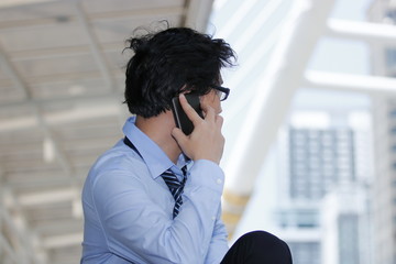 Side view of handsome young Asian businessman talking mobile smart phone at urban building background. Unemployment business concept.