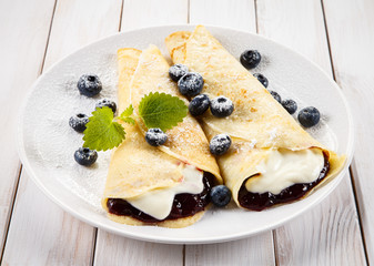 Crepes with blueberries and cream on wooden background 
