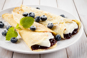 Crepes with blueberries and cream on wooden background 