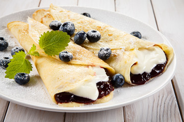 Crepes with blueberries and cream on wooden background 