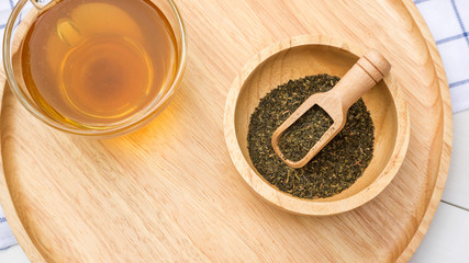 A cup of tea and a green tea leaf on a table.