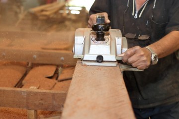 Electric planer shaving a piece of wooden board with hands of senior carpenter in carpentry...