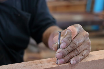 Hands senior carpenter holding nail on wooden piece with copy space.
