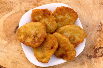 Homemade potato pancakes. Potato fritters on white plate on wooden brown background. Top view.