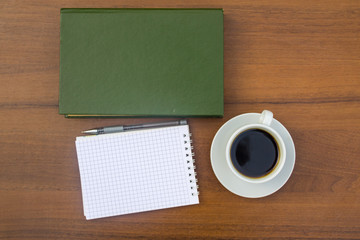 Cup of coffee, book, notepad and pen on wooden desk