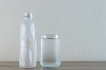 glass of water with plastic water bottle on wooden table.