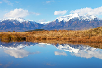 A picturesque landscape with a mirror image of a snow-covered mountain range and sky in calm blue water