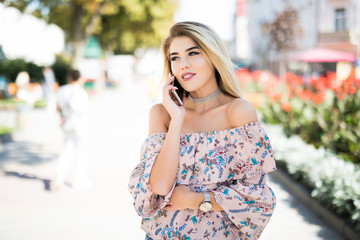 Woman talking by phone outdoors in city street. Portrait of young smiling girl standing with smartphone