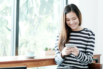 Young asian woman using smart phone while sitting by window cafe background, People technology and lifestyle