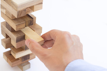 hand of businessman pulling out or placing wood block on the tower