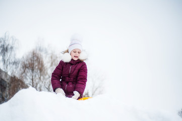 Fototapeta na wymiar A girl in winter clothes is standing with an ice cap on top of a snow hill