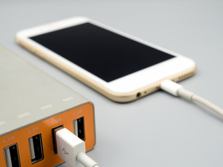 Close-up image of smart phone charging with multiport USB power adaptor on gray background, Selective focus