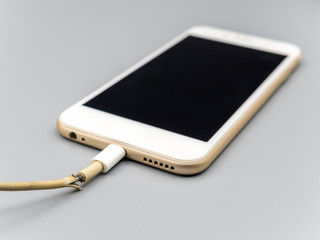 Close-up image of damaged charger cable connecting with smartphone on gray background