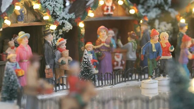 Close-up - miniature souvenir Christmas toy - little people skate in circle on an ice rink illuminated with garland with winter scenery