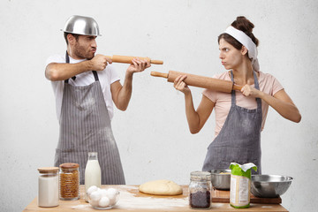 Serious cook competitors pretend that rolling pin is gun, look at each other as on shooting mark, try to prove rightness or case, stand at kitchen table with ingredients and hand made pastry