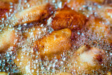 Close up fried chicken wings in boiling oil, in a cast iron frying.