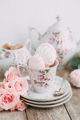 tea set in composition with flowers and marshmallows. Coffee mug on a saucer, a teapot and a sugar bowl. Filmed in the interior