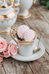 tea set in composition with flowers and marshmallows. Coffee mug on a saucer, a teapot and a sugar bowl. Filmed in the interior