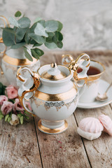 tea set in composition with flowers and marshmallows. Coffee mug on a saucer, a teapot and a sugar bowl. Filmed in the interior