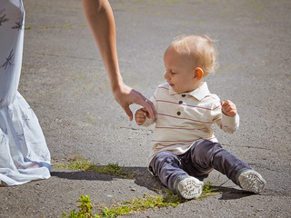 Mother reaches out to the kid sitting on the pavement.