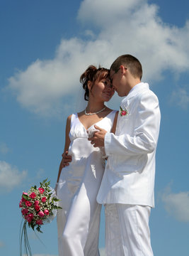 the groom holds the bride's hand against the blue sky