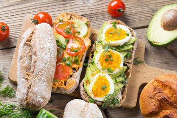 Sandwiches with avocado, eggs and tomato on a wooden background. Fresh organic vegetables, eggs and whole wheat bread. Healthy breakfast. Retro style.