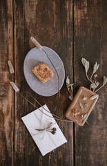 Top close up view of still life with handmade organic rustic soap with dried flowers, soap-dish and little white cute romantic envelope on dark wooden table background. Vertical shot.