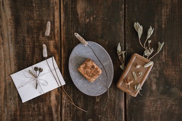 Top view of still life with handmade organic rustic soap with dried flowers, soap-dish and little white cute romantic envelope on dark wooden table background.