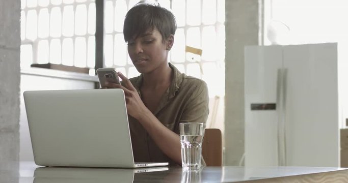 Attractive latina black woman wearing casual silk button up top typing on a laptop in a modern lof style office