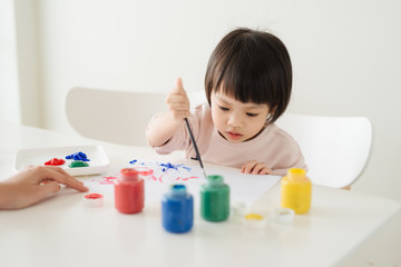 Little asian girl painting with paintbrush and colorful paints