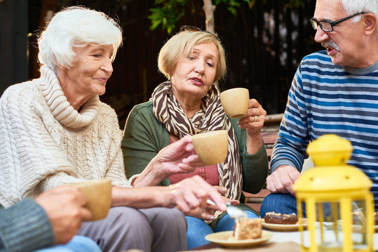 Elderly people wearing warm clothes enjoying each others company while having tea party with delicious cake outdoors