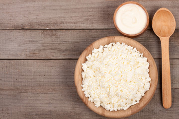 Cottage cheese in a wooden bowl with sour cream on old wooden background with copy space for your text. Top view