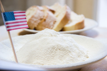 Close-up shot of american flag and flour in a plate. Slices of bread on the background