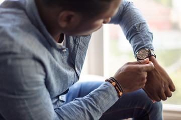 Handsome african man looking at his watch while sitting in his home or office