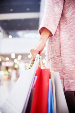 Closeup of young woman holding paper bags with purchases while shopping in mall