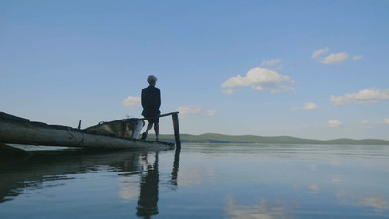 Naklejka premium Side view of a girl sitting on wooden pier on river bank. Side view of dreaming girl sitting on wooden pier on river bank. Beautiful woman with blond hair