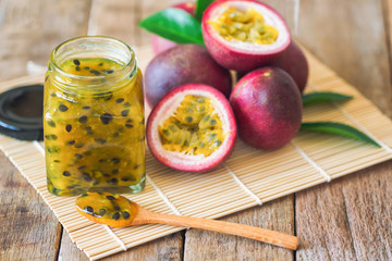 Homemade passion fruit jam in bottle put on wood table. Passion fruit jam background with copy space for your design. Fresh passion fruit and homemade jam on wood table in natural tone style concept.