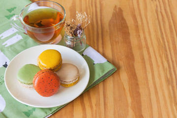 Colorful French macaron or Italian macaron on white plate. Homemade delicious macaron and tea on wood table with copy space for background or wallpaper. Macaron is popular dessert for served with tea.