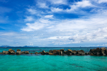 Fototapeta na wymiar Dam rock on the sea with blue sky and clouds.