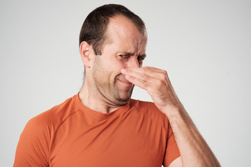 Caucasian man is pinching nose with fingers and looking with disgust because of bad smell isolated on white background