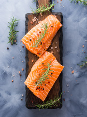Raw salmon pieces on wooden board with herbs, salt and spices